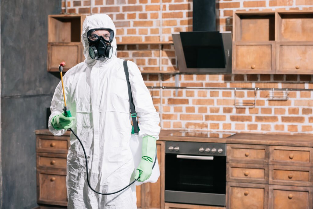 pest control worker standing with sprayer in kitchen